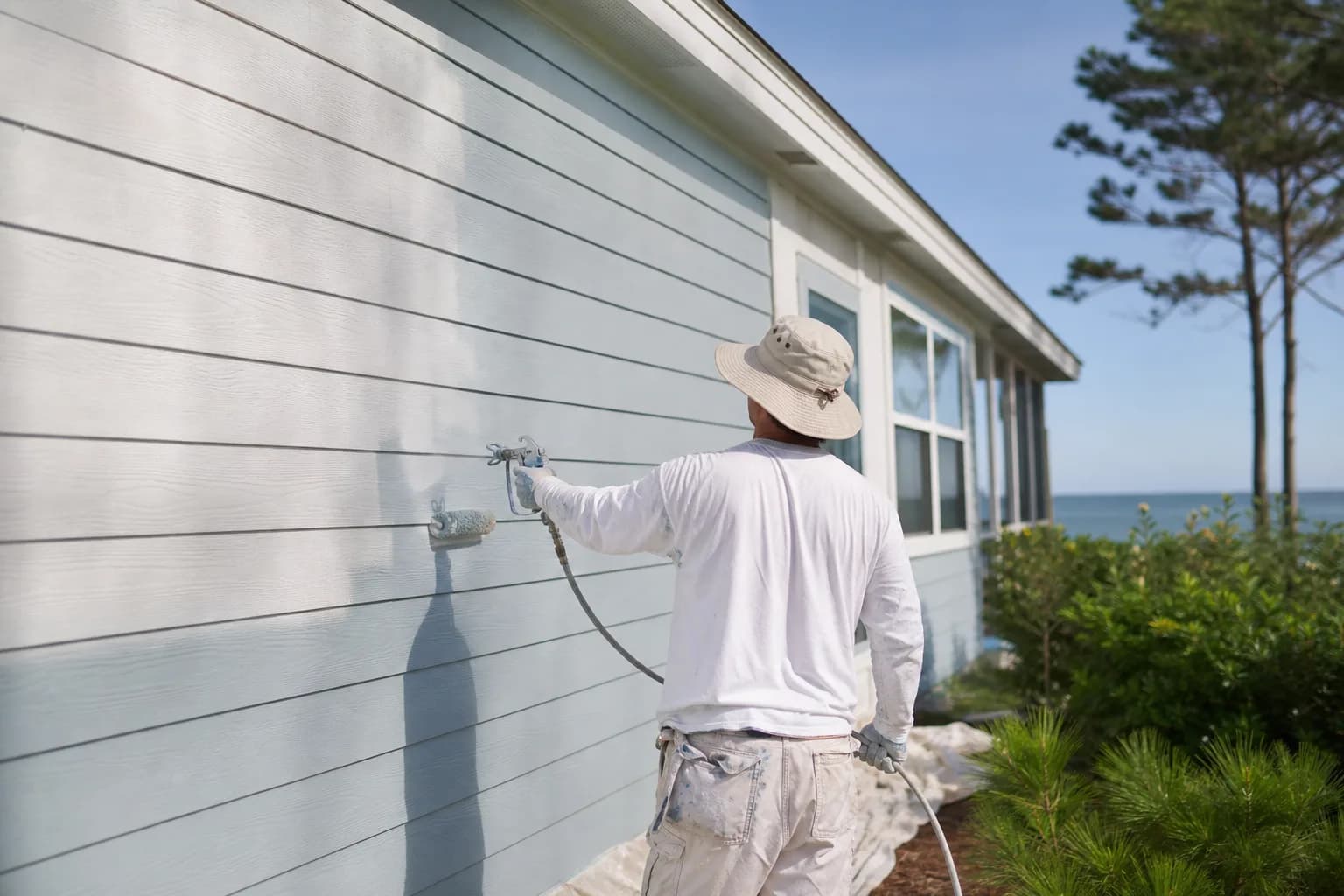 Painter applying fresh paint to fiber cement lap siding on a coastal Alabama home, showing that fiber cement siding can be repainted