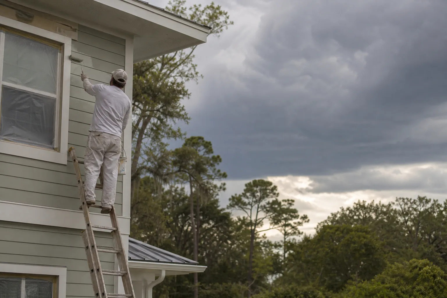 Painter finishing an exterior coat ahead of an approaching Gulf Coast storm, racing the dry-time window before rain