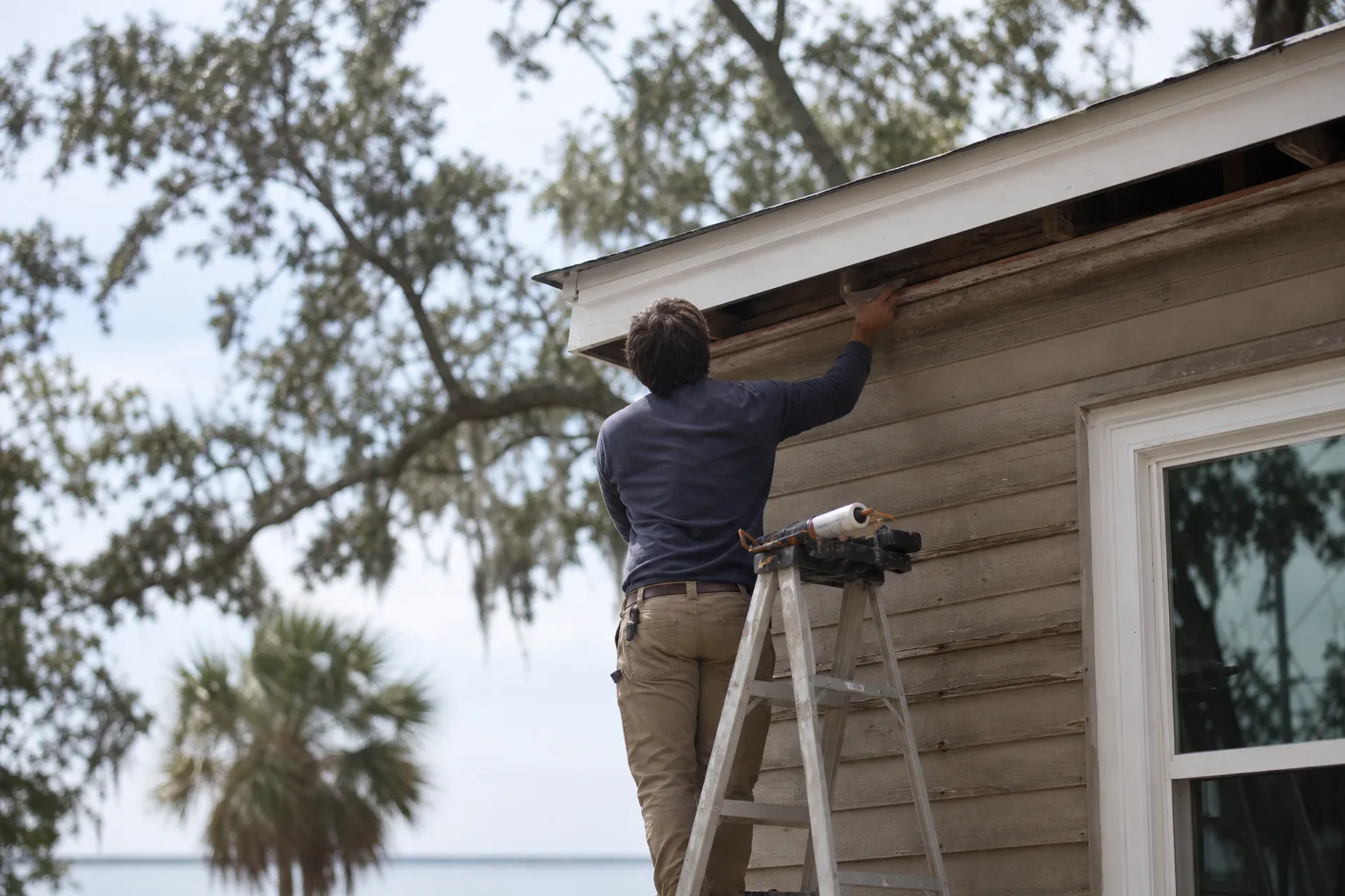 Carpenter replacing rotted exterior fascia before painting on a Gulf Coast home