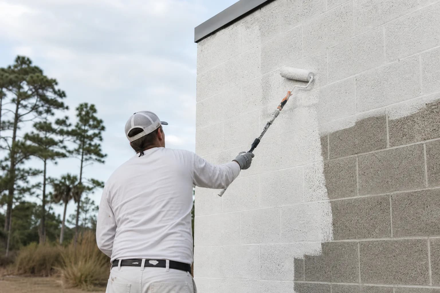 Painting a cinder block wall on a Gulf Coast building: block filler being rolled into the open pores of a CMU wall before topcoat