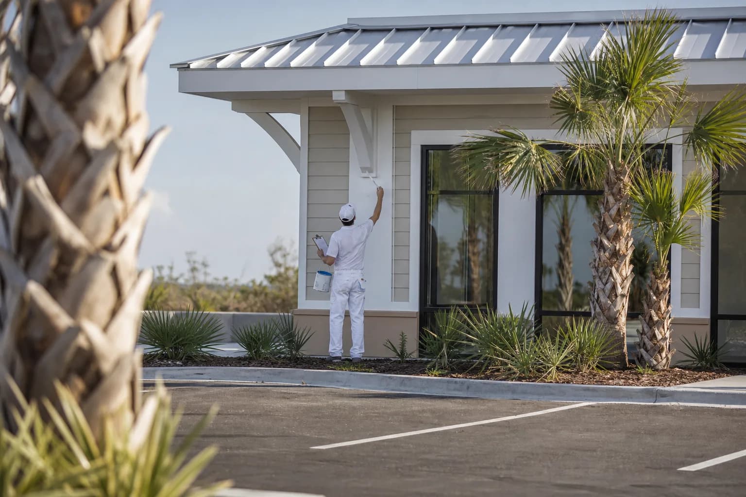 Painter inspecting and touching up the exterior of a Gulf Coast commercial building as part of a paint maintenance program