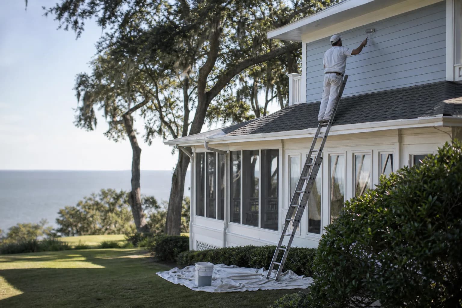 Painter on a ladder repainting a two-story Spanish Fort, Alabama home, illustrating exterior house painting cost on the Eastern Shore