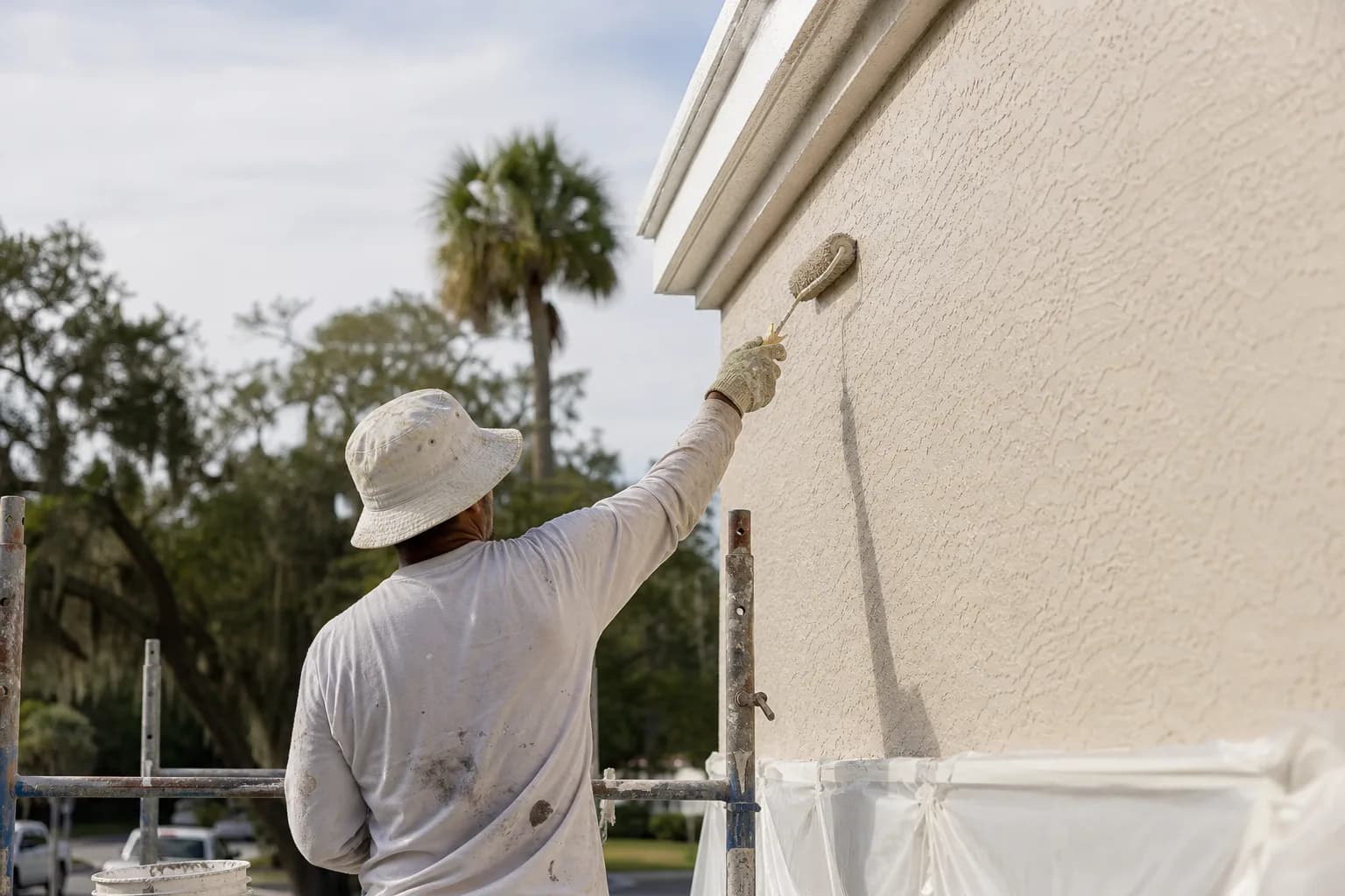 Painter rolling a thick coating onto a textured stucco exterior wall on the Gulf Coast