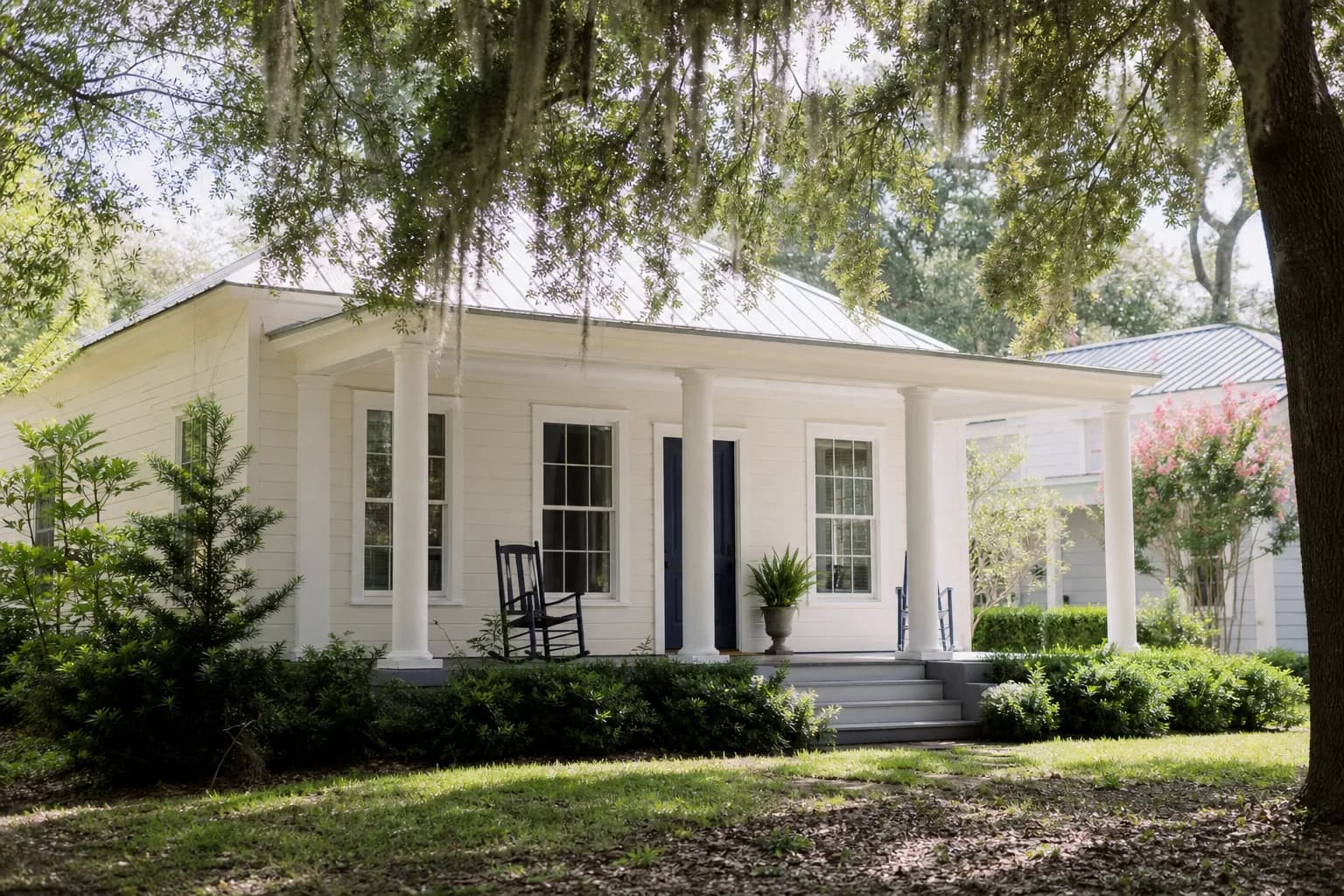 Mobile coastal cottage painted soft white with white trim and a navy door under live oaks