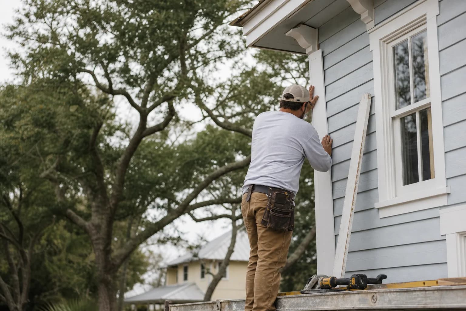 Carpenter fitting a new primed exterior corner board before painting, illustrating exterior trim repair as paint prep