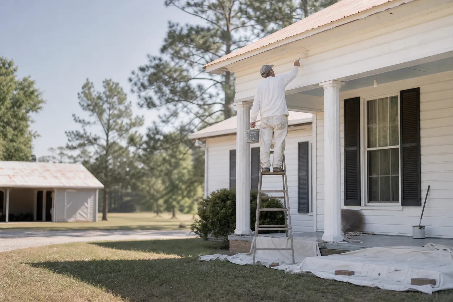 House painter repainting an older rural farmhouse with a wide porch in Citronelle, AL
