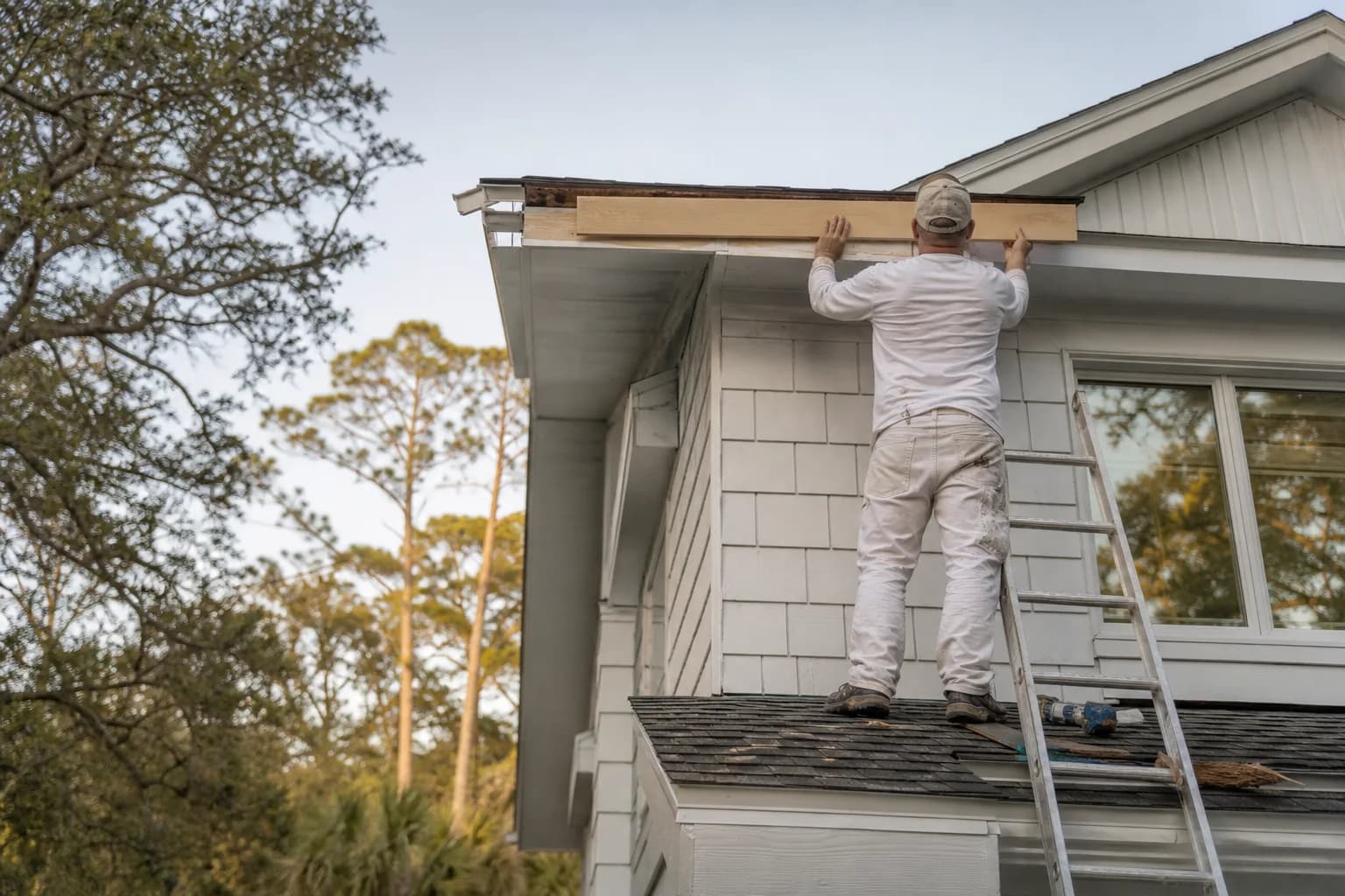 Painter replacing a rotted fascia board before exterior painting, illustrating carpentry on a paint quote