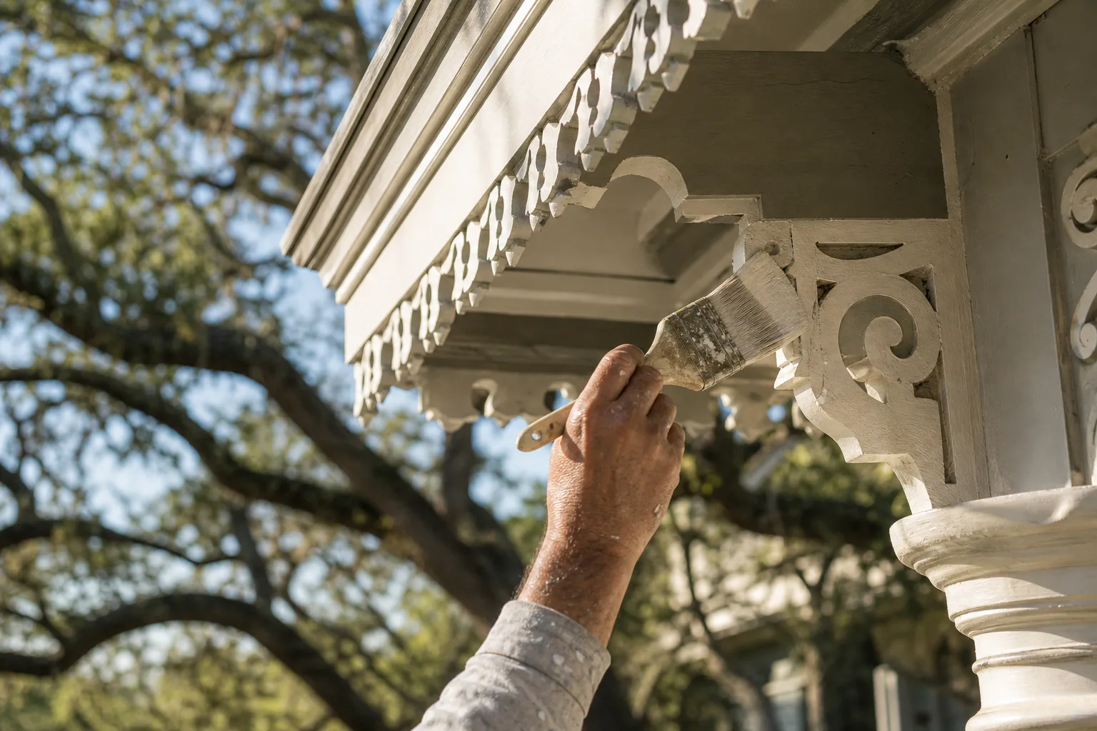 Painter hand-brushing ornate Victorian eave brackets and gingerbread trim on a historic home