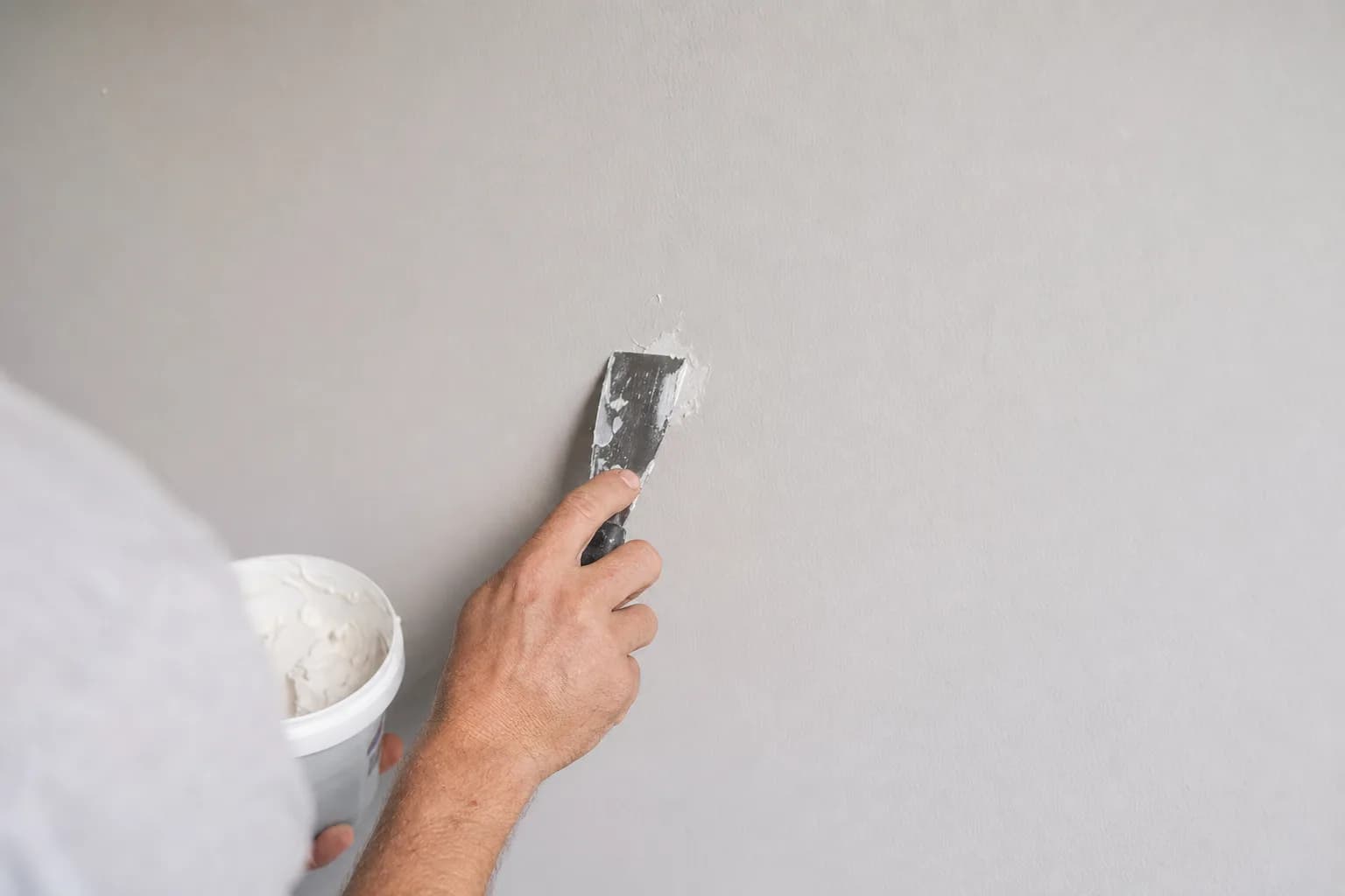 Hand applying spackle to a nail hole in a wall with a putty knife