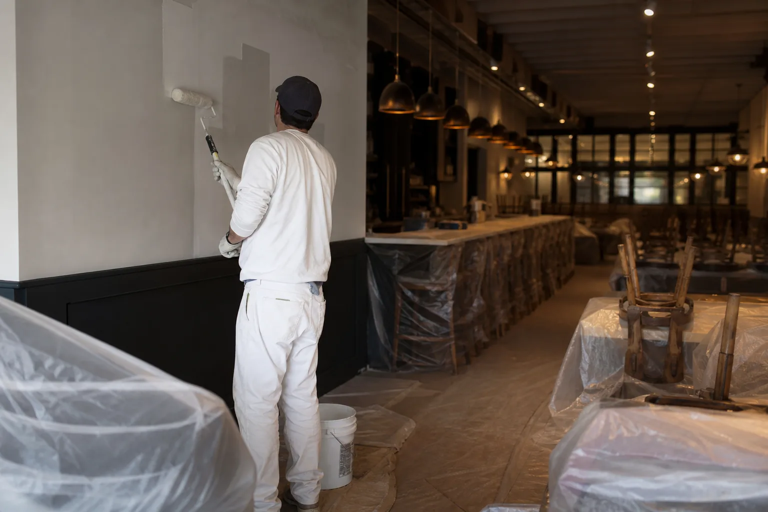 Restaurant painting in Mobile after service hours: rolling fresh paint on a dining-room wall with tables wrapped and chairs stacked