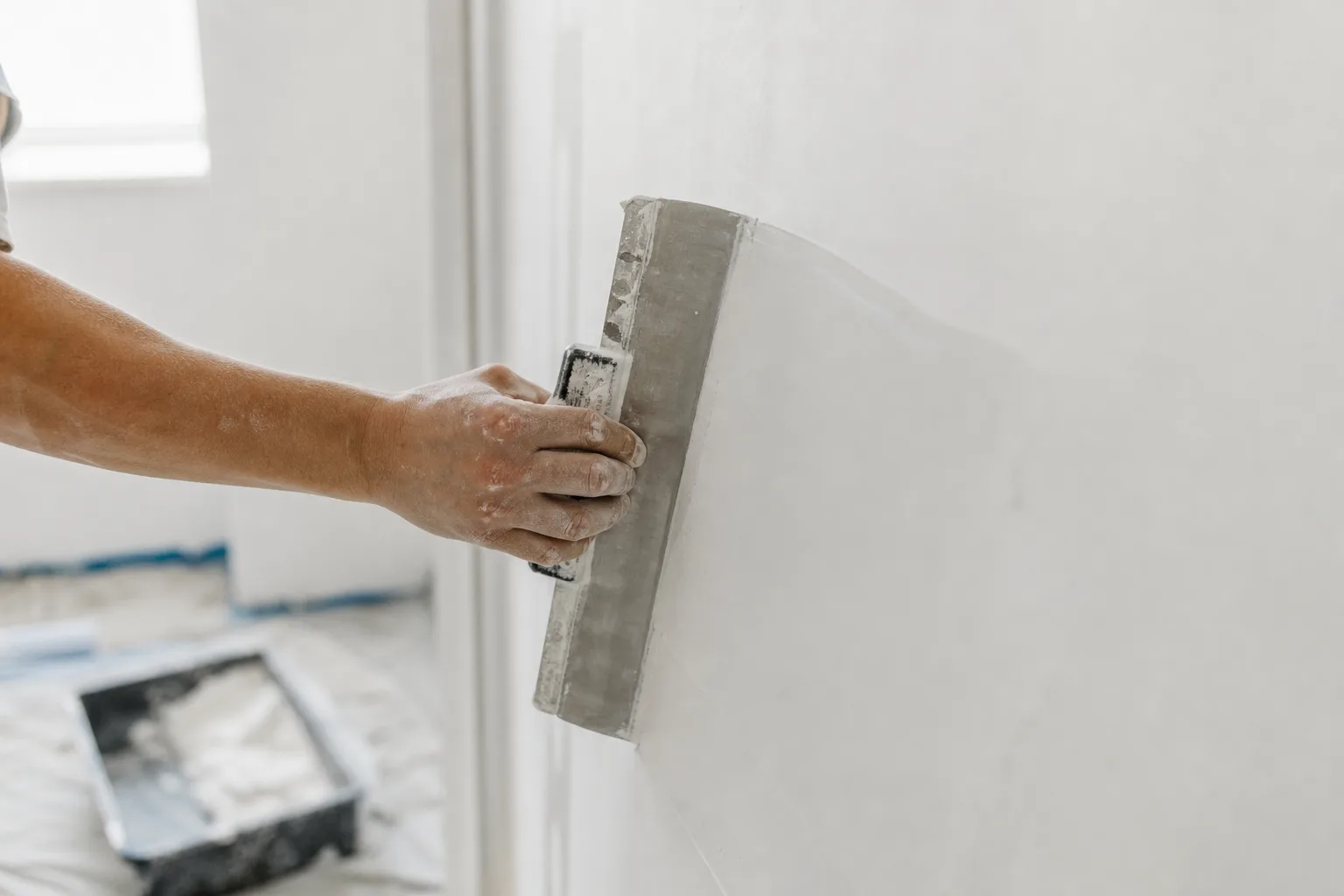 Spreading a thin skim coat of joint compound across a wall with a wide trowel for a smooth, paint-ready finish