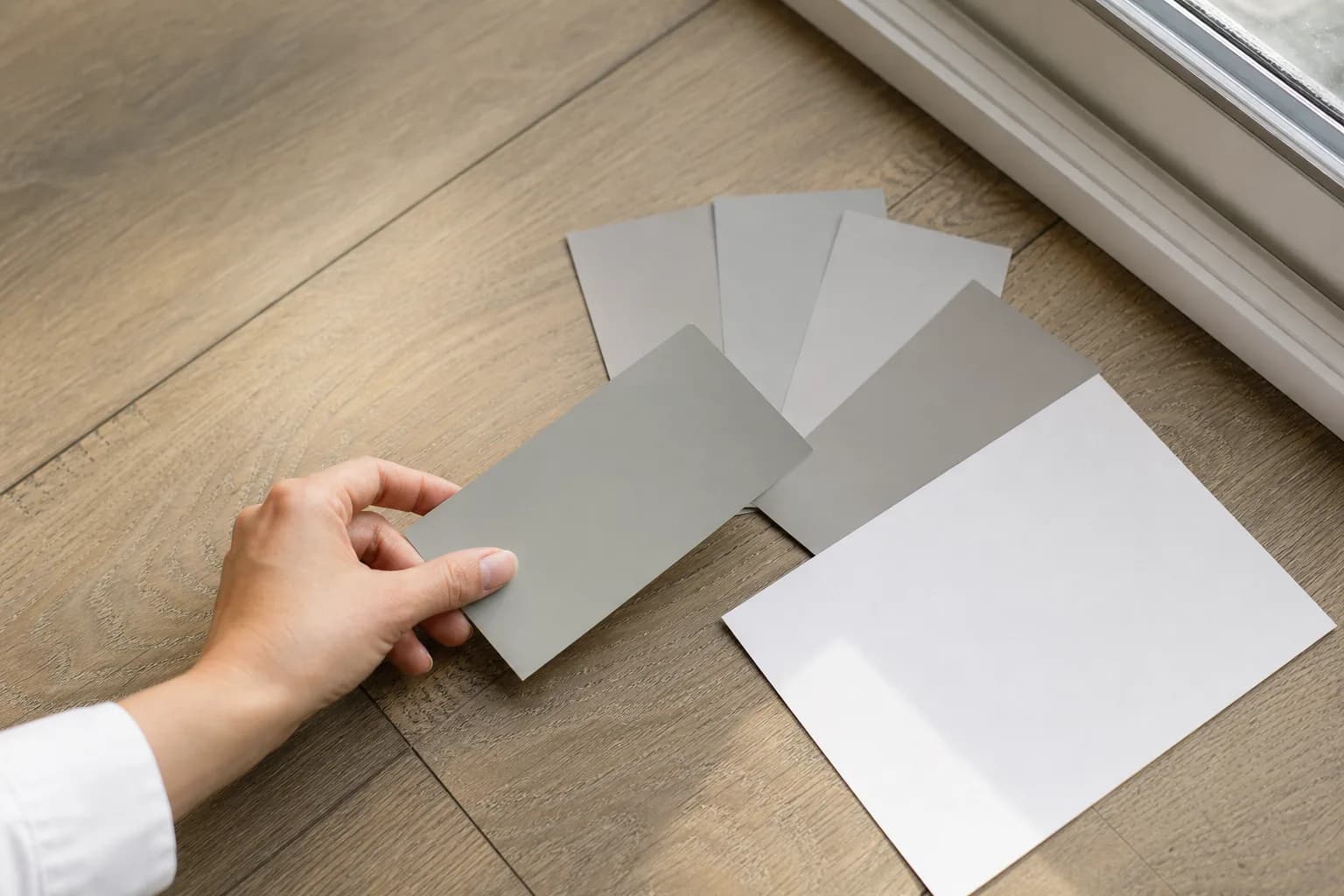 Gray and greige paint swatches on a wood floor beside a white card, showing how to spot paint undertones