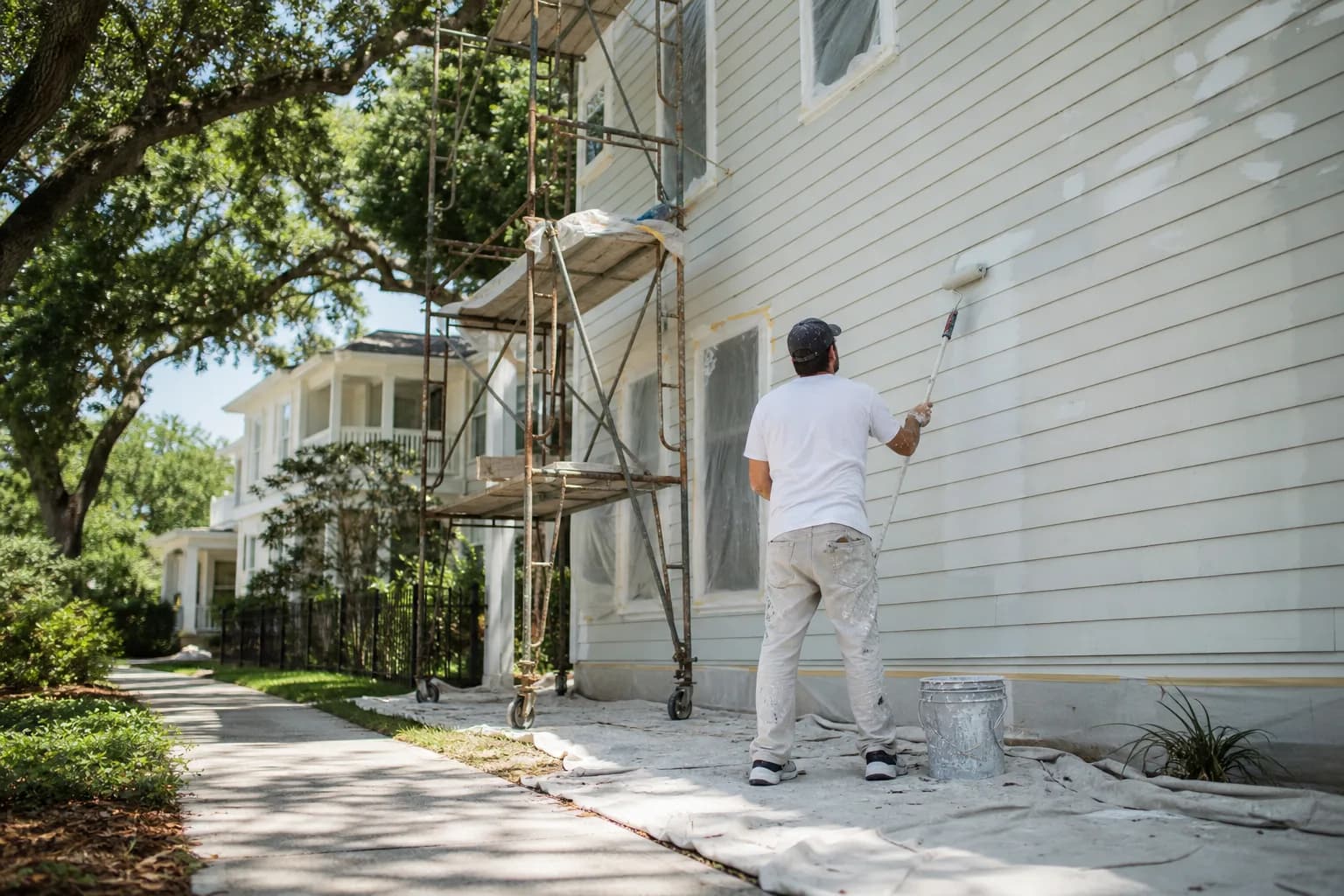 A painter rolling a freshly prepped exterior wall on a Gulf Coast home, illustrating the factors that drive house painting cost