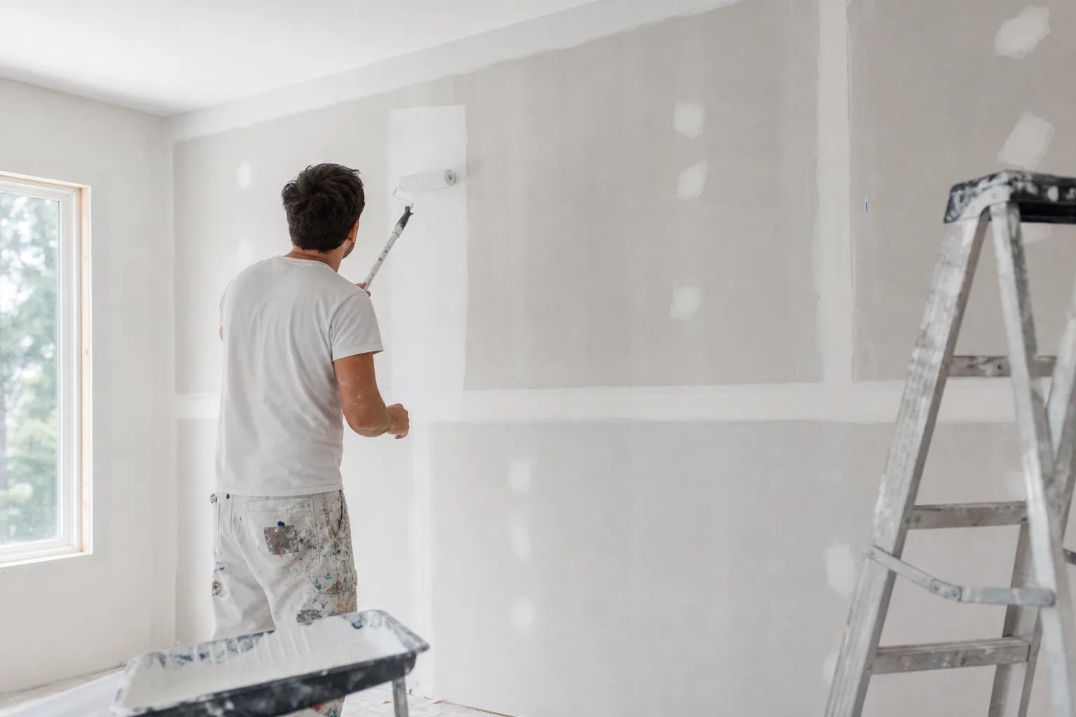 Painter priming new interior drywall walls before painting, showing when walls need primer first